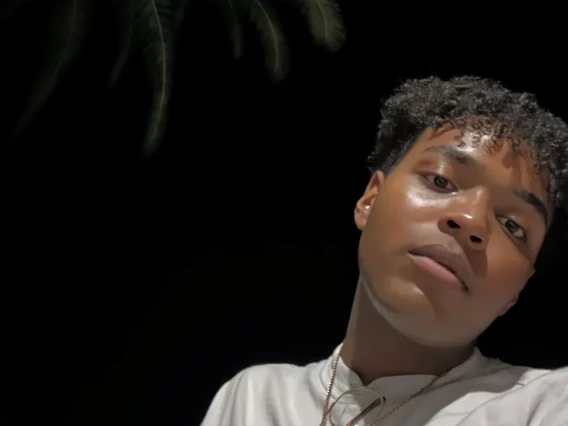 Jarmon in the bottom right corner of a dark nighttime sky, with the outline of a palm tree to his left. He is tilting his head and looking down at the camera.
