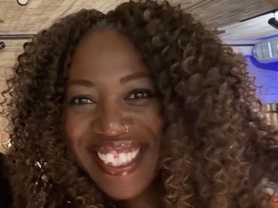 Smiling Black woman with curly light brown hair.