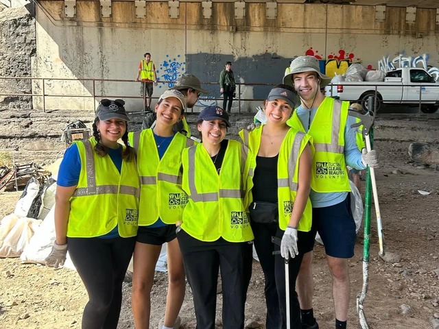 5 students wearing bring yellow vests holding shovels and other tools