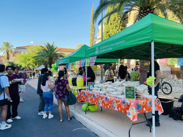 2 green tents set up outside, food on tables under them, students lined up