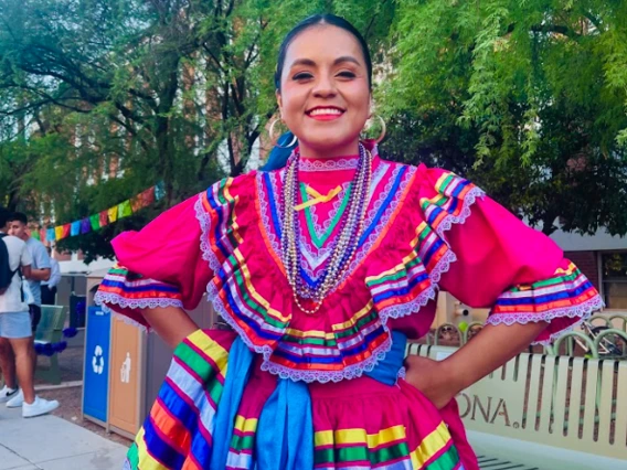 Folklorico Dancer wearing a traditional bright pink dress with colorful ribbons