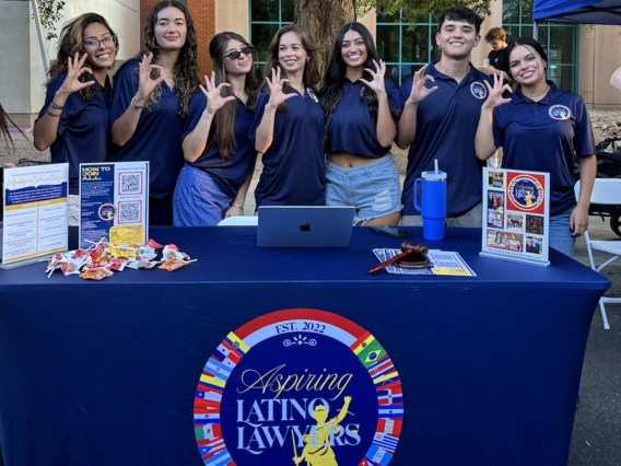 Students standing in front of a table, students are wearing blue polos, they are holding the wildcats sign with their hand