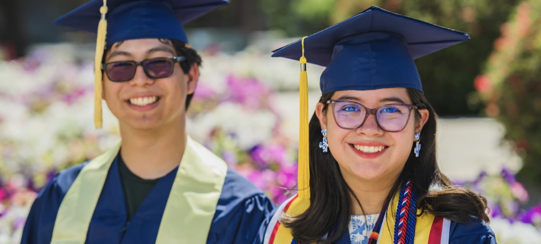 2 students sitting on a bench with graduation regalia on