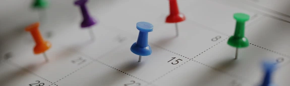 A white calendar with different colored push pins in it