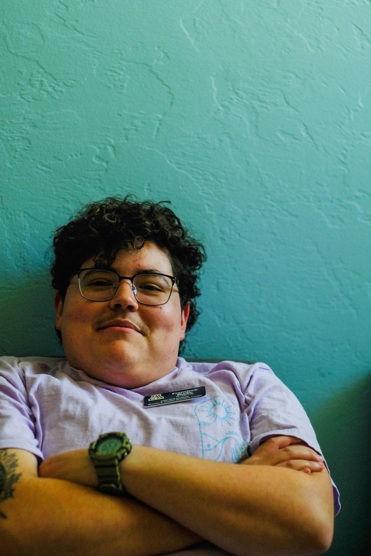 Francisco leaning back with his arms folded, sitting against a teal wall. He is smiling at the camera.
