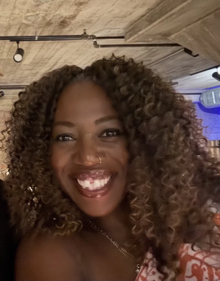 Smiling Black woman with curly light brown hair.