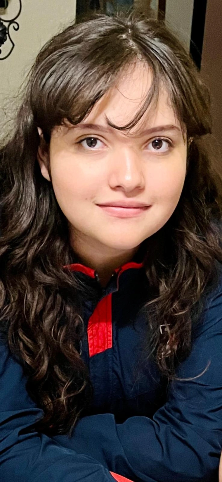 Anis smiling at the camera with her hair pulled over her shoulders, and her bangs curled slightly on her forehead.