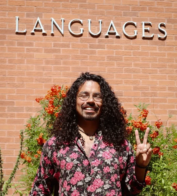 Image of professor standing in front of building holding a peace sign 