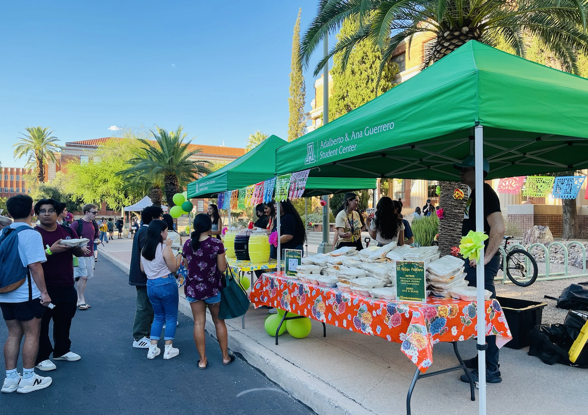 2 green tents set up outside, food on tables under them, students lined up